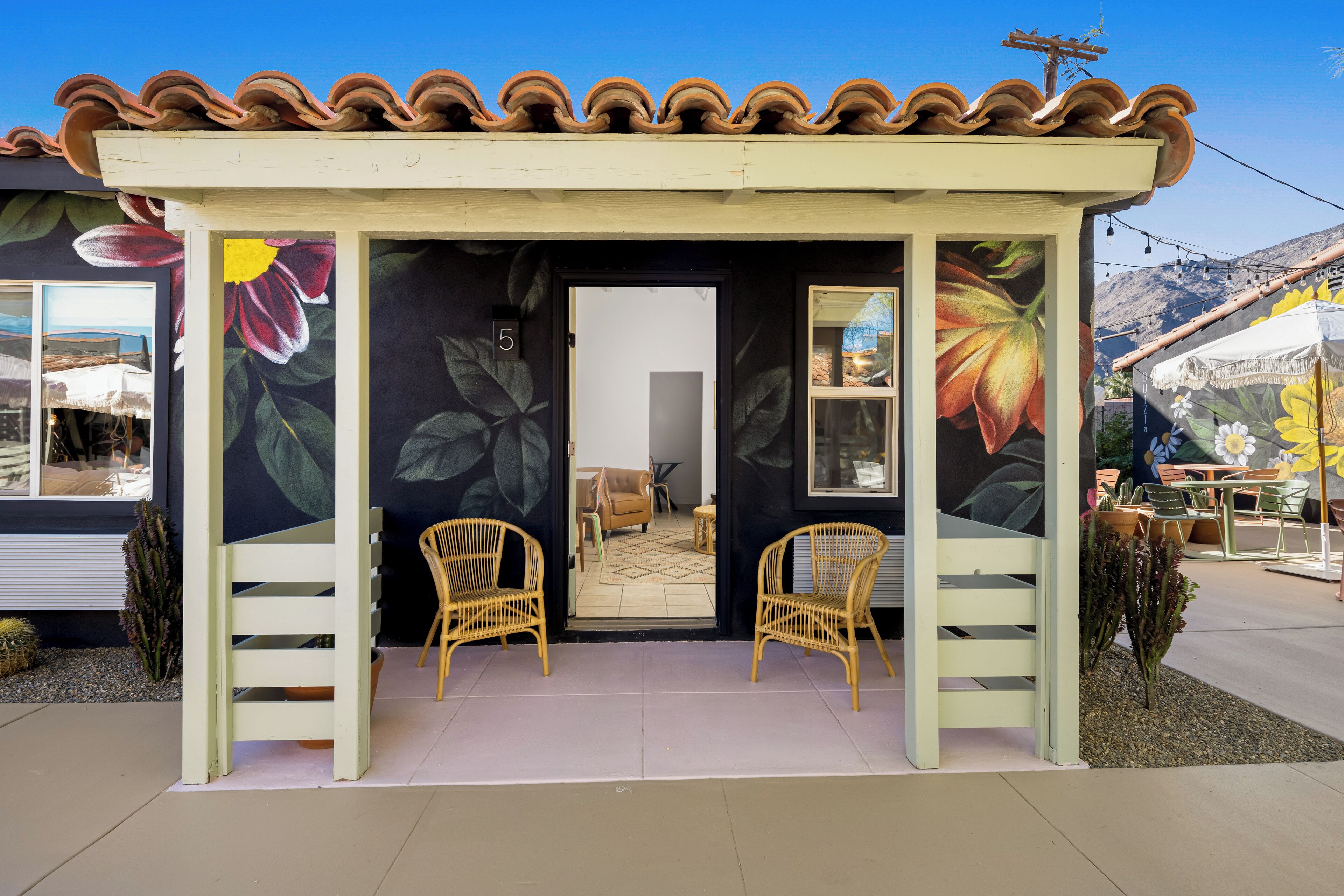 A covered outdoor seating area with wicker chairs and a door leading to an interior space.