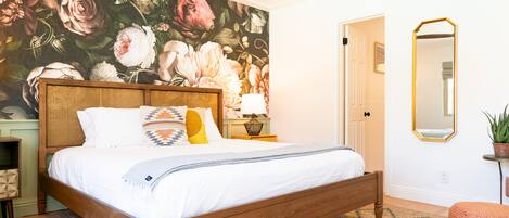 Une chambre avec un grand décor mural floral, un lit en bois, une table de chevet avec une lampe et un miroir au mur.