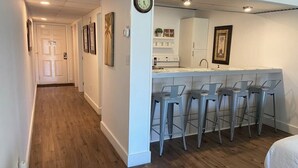 A kitchen with a bar area, wooden flooring, and a clock on the wall.