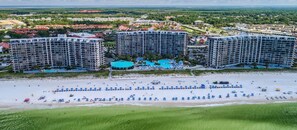 Resort com vários edifícios altos, área de piscina central e praia com vários guarda-sóis e espreguiçadeiras.