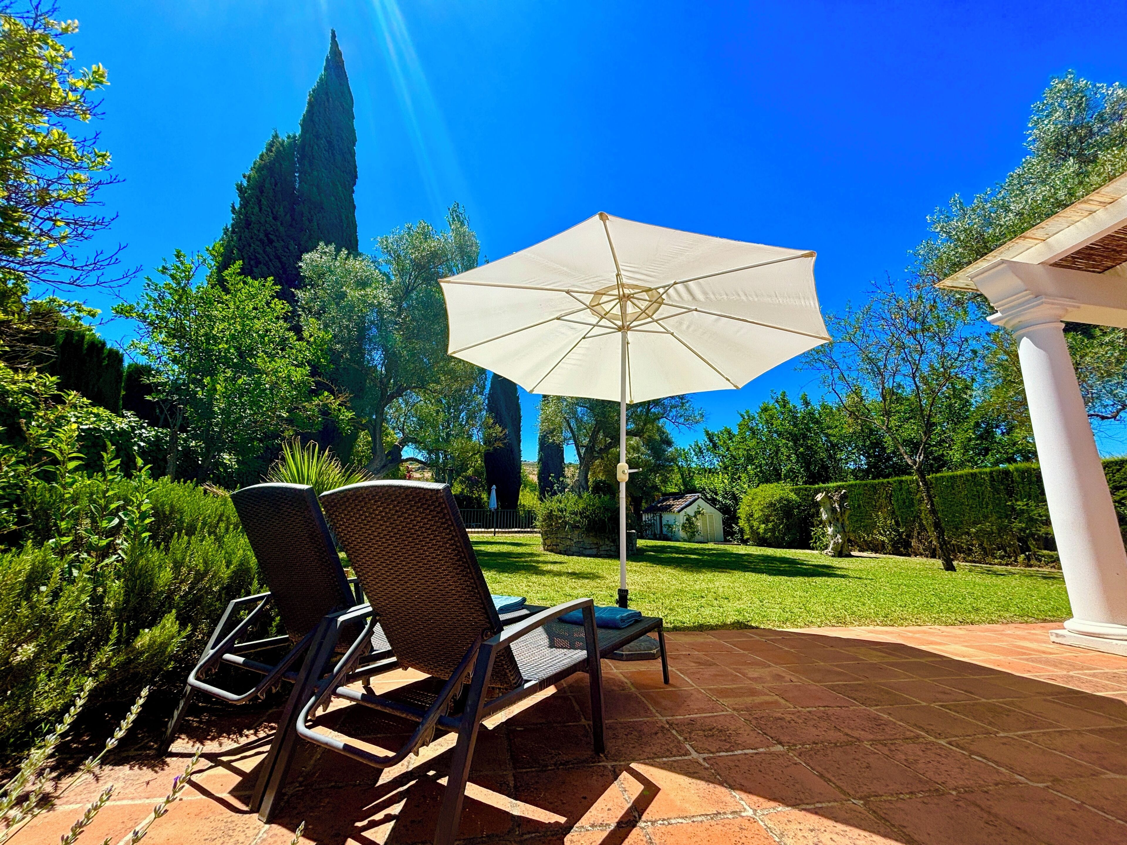 Une terrasse avec deux fauteuils en osier, un parasol blanc et un chemin en pierre.