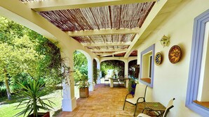 Un patio al aire libre con suelo de baldosas, sillas de madera, una mesa y plantas en macetas.