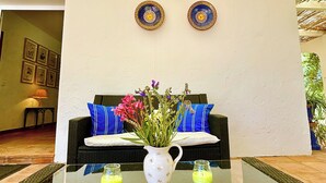 Una habitación con una mesa de vidrio, dos platos decorativos, un sofá de mimbre y una planta en maceta.