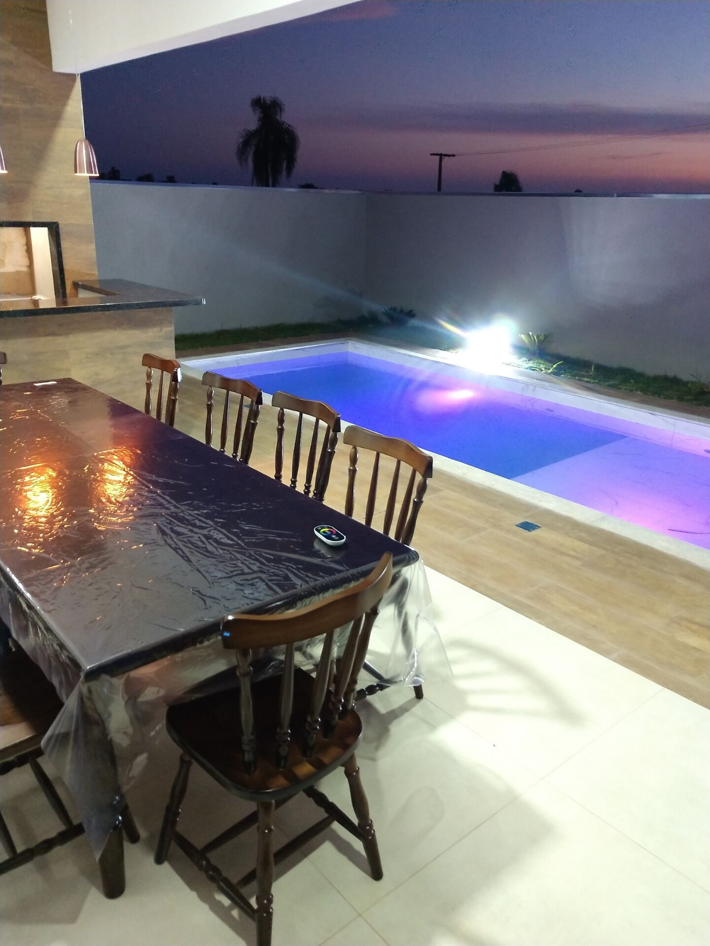 Un espace repas avec une table et des chaises, une piscine à l’eau bleutée et une vue sur le ciel.
