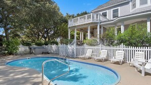 A swimming pool with a white fence and lounge chairs, surrounded by trees and a house with a balcony. - 8th And Sound: Elevator | Pool | Hot Tub (Corolla)