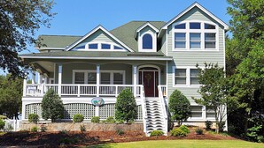 A two-story house with a front porch, a stone retaining wall, and a well-maintained lawn. - 40-Love is a:  Soundfront | Private Pool | Spa (Corolla)