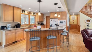 A spacious kitchen with wooden cabinets, a central island with bar stools, and pendant lighting. - 40-Love is a:  Soundfront | Private Pool | Spa (Corolla)