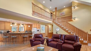 A spacious living area with a wooden staircase, leather sofas, and a kitchen with wooden cabinets and a bar. - 40-Love is a:  Soundfront | Private Pool | Spa (Corolla)