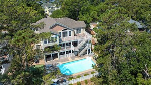 Uma casa grande com piscina, rodeada por árvores e vista para a água.