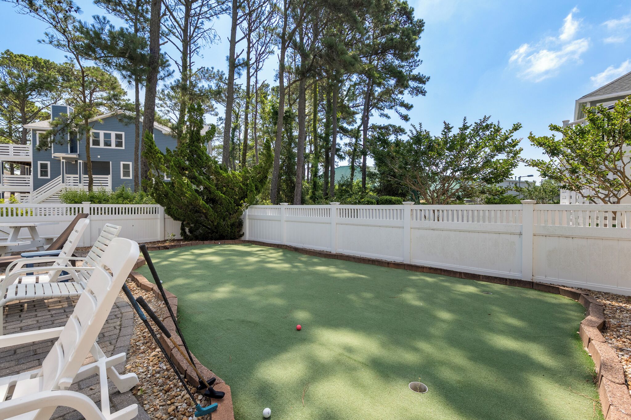A backyard with a green artificial turf, white lounge chairs, and a white picket fence.