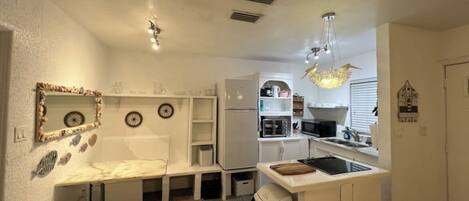 Una cocina compacta con muebles blancos, un microondas integrado, un lavamanos y una pequeña isla con tabla de cortar.