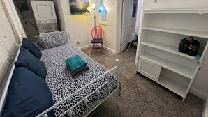 Une petite chambre à coucher avec un lit, une chaise, une étagère et un radiateur.