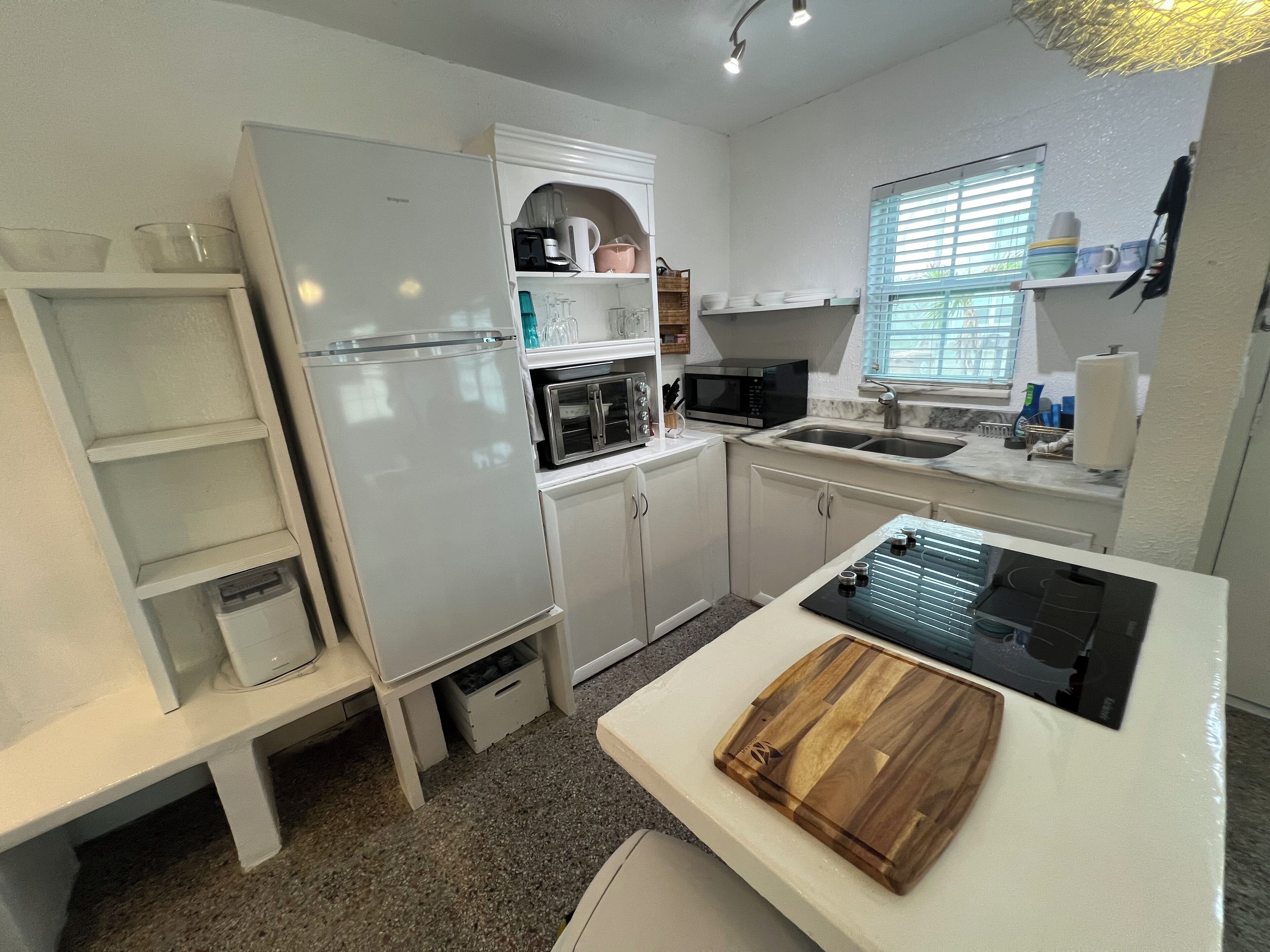 A compact kitchen with white cabinets, a built-in microwave, a sink, and a countertop with a cutting board.
