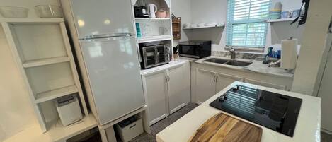 A compact kitchen with white cabinets, a built-in microwave, a sink, and a countertop with a cutting board.