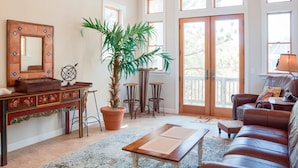 A living room with a large window, a potted plant, a wooden coffee table, a brown leather sofa, and a decorative mirror. - Reminiscent: Oceanside, Private Pool, Spa (Nags Head)