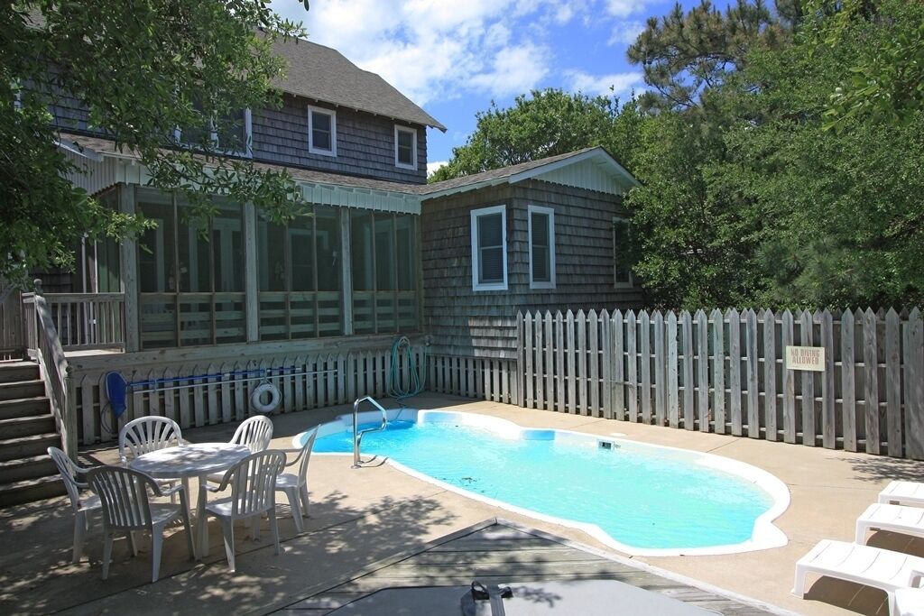 Un jardin avec une piscine, une terrasse couverte et une clôture en bois.