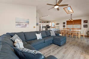 Ein modernes Wohnzimmer mit einer Eckcouch, einem Essbereich mit Holzkästen und einer Küche im Hintergrund.