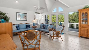 A spacious living room with a high ceiling, wicker furniture, and a large window offering a view of the outdoors. - Treasured Dreams: Private pool, Short Drive to Beach, Great Community Amenities! (Corolla)