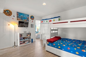 Ein Kinderzimmer mit Etagenbett, Bücherregal, Fernseher und einem Fenster mit Vorhängen.