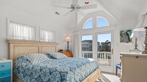 A bedroom with a large bed, a ceiling fan, a window with curtains, and a view of buildings outside. - Treasured Dreams: Private pool, Short Drive to Beach, Great Community Amenities! (Corolla)