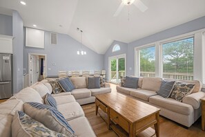 A spacious living room with a large sectional sofa, a wooden coffee table, and a dining area with chairs.