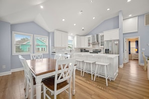 A modern kitchen with white cabinetry, a central island, and a dining area with white chairs.