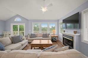 A spacious living room with a ceiling fan, a fireplace, and a television mounted on the wall.