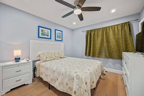 A bedroom with a bed, bedside tables, a ceiling fan, and a window with curtains.
