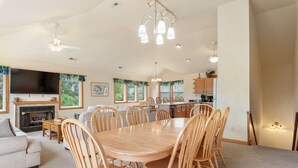 Un vaste salon comprenant une grande table à manger en bois, entourée de chaises, une cheminée et un téléviseur.