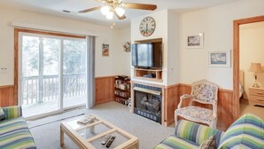 A living room with a ceiling fan, a television, a fireplace, and a large window with a view of the outdoors. - A Dolphin's Cove: Rec Room w/ Pool Table, Private Pool & Spa, Dogs OK! (Corolla)