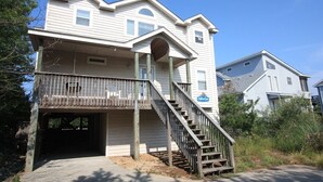A two-story house with a covered front porch and a staircase leading to the entrance. - A Dolphin's Cove: Rec Room w/ Pool Table, Private Pool & Spa, Dogs OK! (Corolla)