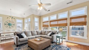 A spacious living room with a large sectional sofa, a round coffee table, and a ceiling fan. - Craba-Cabana: Surf, Sand, and a Private Pool; Community Pool and Tennis Court (Corolla)