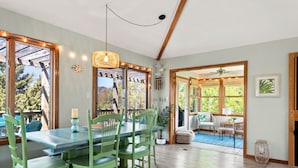 Un espace repas avec une table en bois et des chaises vertes, un luminaire suspendu et une vue dégagée grâce à de grandes fenêtres.