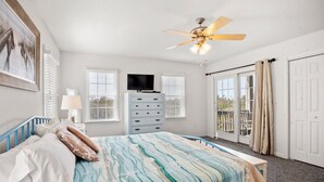 Quarto com cama, cómoda, ventoinha no teto, televisão e porta de correr de vidro.