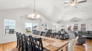 Uma sala de estar espaçosa com uma mesa de jantar, cadeiras e um sofá cinzento.