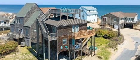 Une propriété située en bord de mer, comprenant plusieurs bâtiments, notamment une grande maison en bois dotée d’un balcon et une plus petite maison bleue.