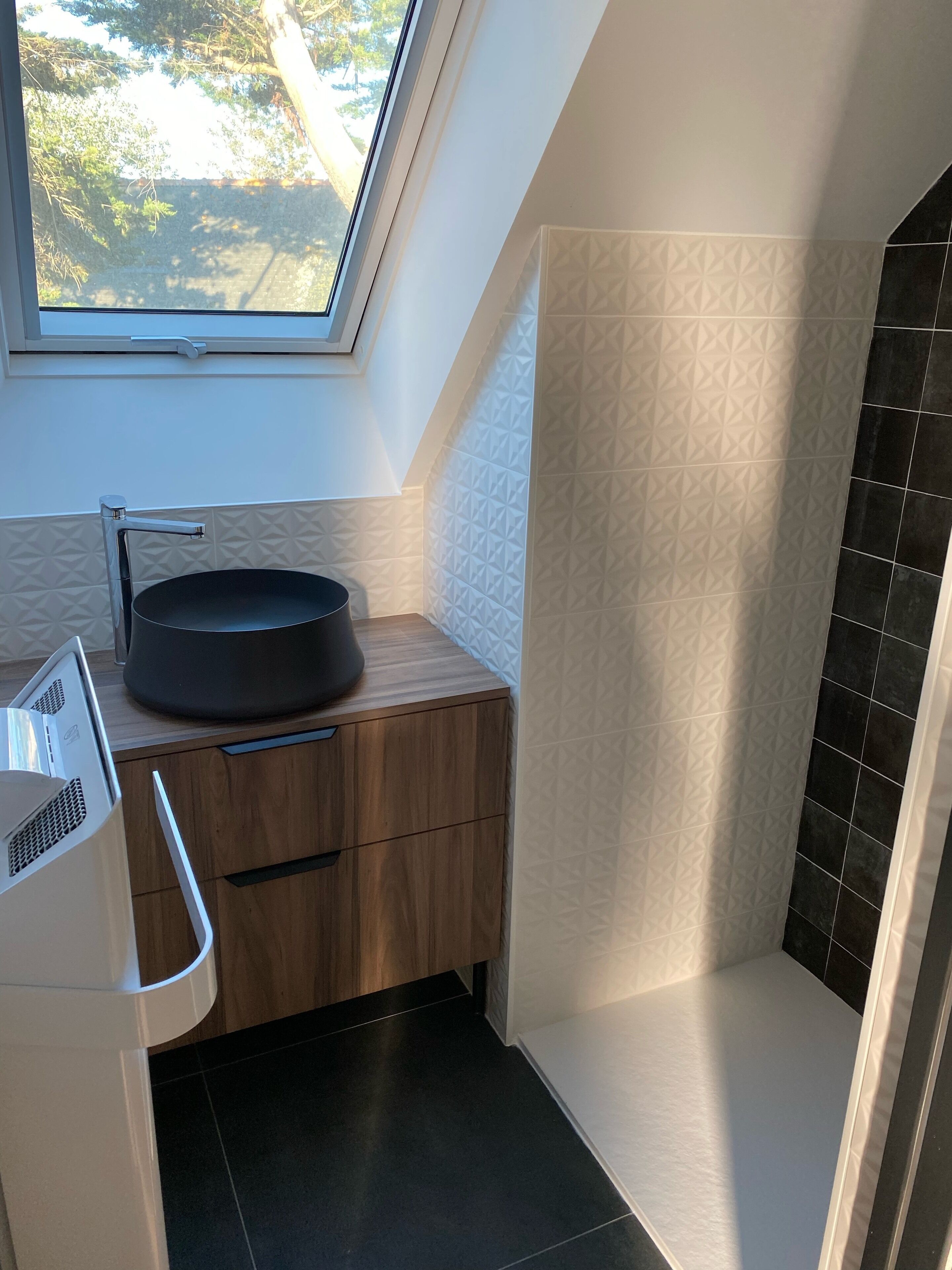 Une salle de bain moderne dotée d’un puits de lumière, d’un lavabo noir, d’un meuble-lavabo en bois et de murs aux motifs géométriques en noir et blanc.