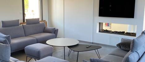 A modern living room with a grey sofa set, a coffee table, and a flat-screen TV mounted on the wall.
