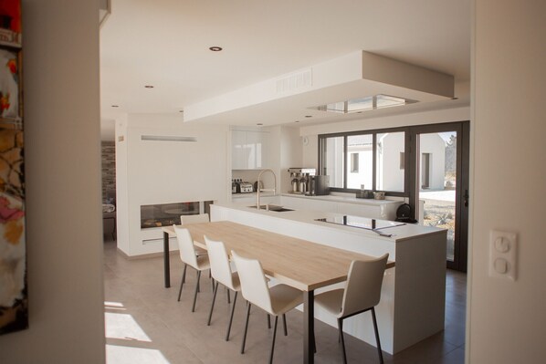 Une cuisine moderne dotée d’un îlot central, de meubles blancs et d’une grande fenêtre qui laisse entrer la lumière naturelle.