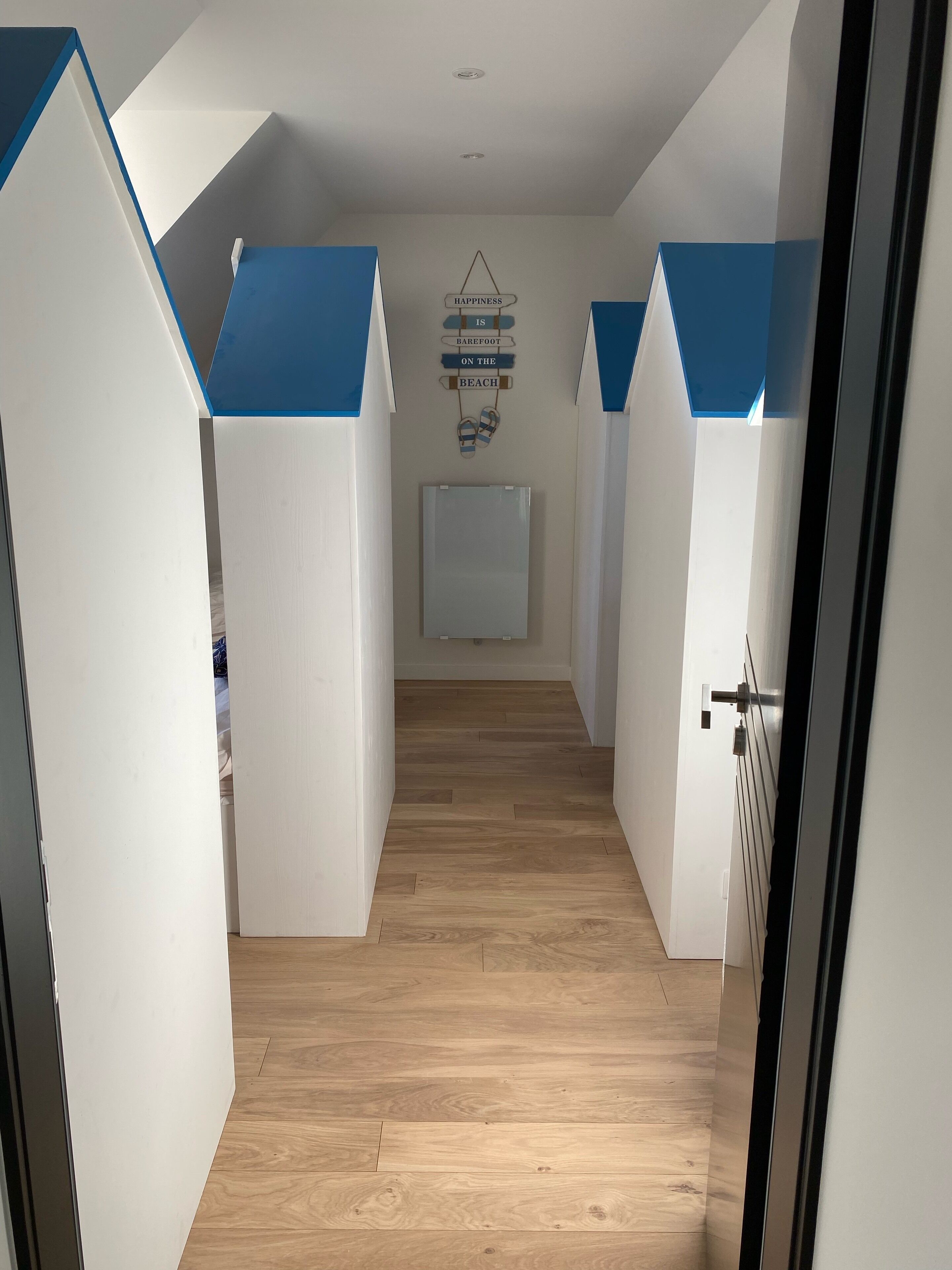 A hallway with white walls and blue accents, leading to a room with a bed and a wall-mounted radiator.