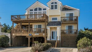 Una casa sulla spiaggia a due piani con un balcone al primo piano e un ingresso separato con un cancello di legno.