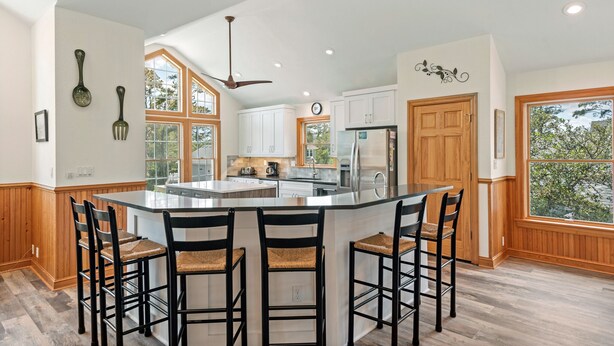 A spacious kitchen with a central island, wooden cabinetry, and a large window providing natural light. - Joyful Sound: Soundside 5-bedroom, Private Pool & Spa, Elevator and Dog-friendly (Corolla)