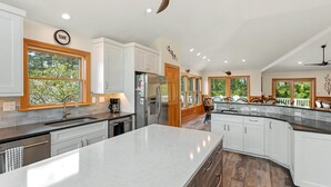 A spacious kitchen with white cabinets, a large island, and a wooden ceiling fan. - Joyful Sound: Soundside 5-bedroom, Private Pool & Spa, Elevator and Dog-friendly (Corolla)