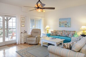 A living room with a beige armchair, a blue sofa, a striped armchair, a coffee table, and a ceiling fan.