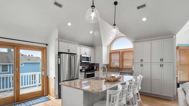 Una cocina moderna con una isla central, armarios blancos, electrodomésticos de acero inoxidable y un amplio ventanal.