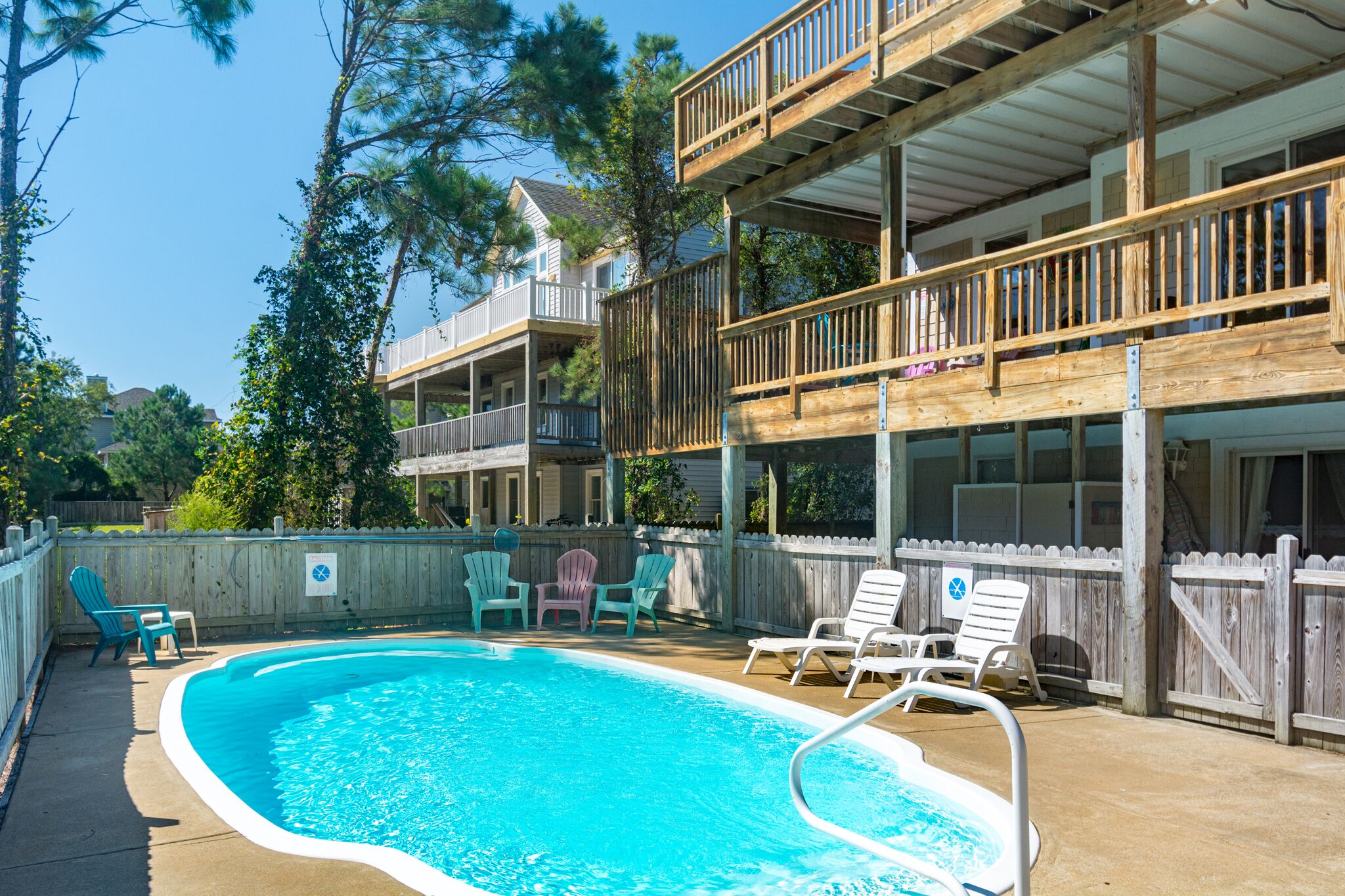 Un espace piscine doté d’une terrasse en bois, de chaises longues et d’un bâtiment à deux étages avec des balcons.