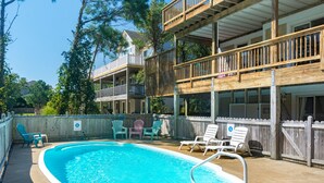 Ein Poolbereich mit Holzterrasse, Liegestühlen und einem zweistöckigen Gebäude mit Balkonen.
