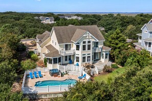 Une grande maison avec une piscine, plusieurs terrasses et une vue sur l’océan.