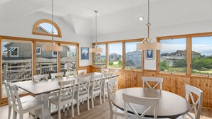 A dining area with wooden walls, large windows, and white furniture. - The Wheelhouse: Pool and Hot Tub | 500ft. to Beach (Corolla)