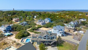 A coastal residential area with multiple houses, a lighthouse, and a large swimming pool. - The Wheelhouse: Pool and Hot Tub | 500ft. to Beach (Corolla)